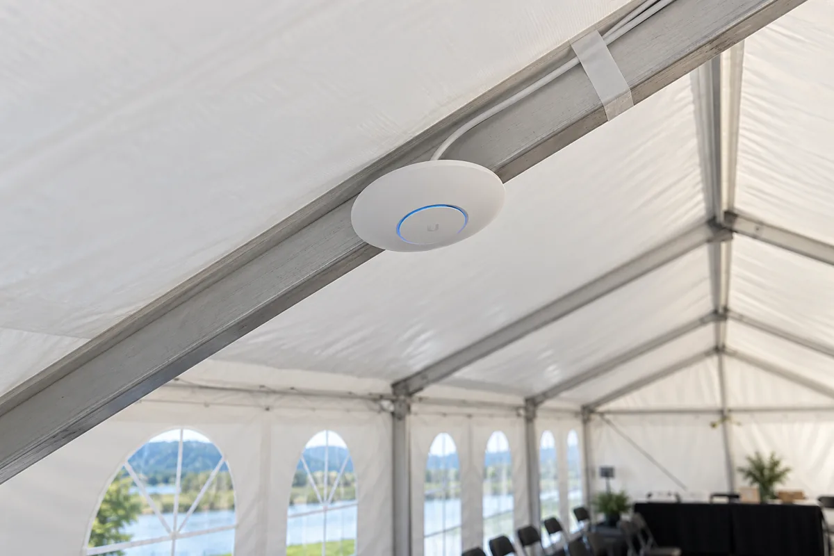 AI-illustrasjon av et aksesspunkt på en skrå aluminiumsbjelke i teltets tak, med kabel teipet langs samme bjelke
